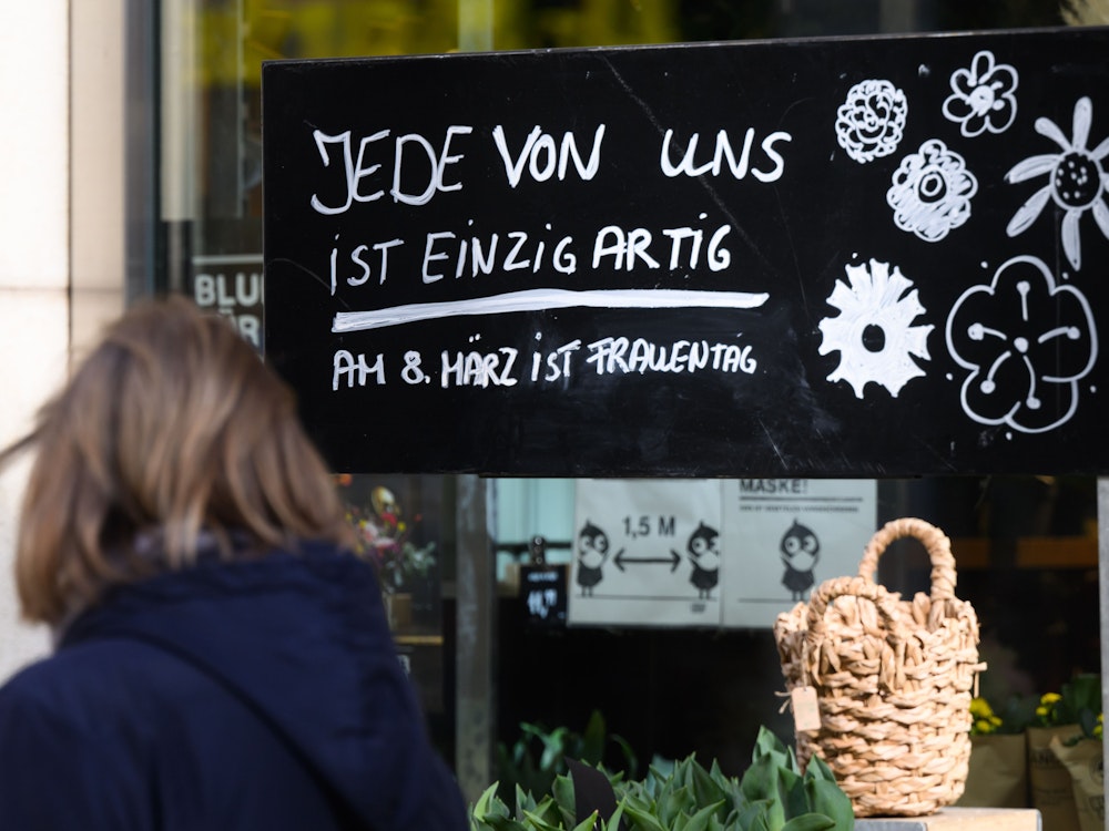 Ein Schriftzug „Jede von ist einzigartig - Am 8. März ist Frauentag“ steht auf einem Schild vor einem Blumenladen.