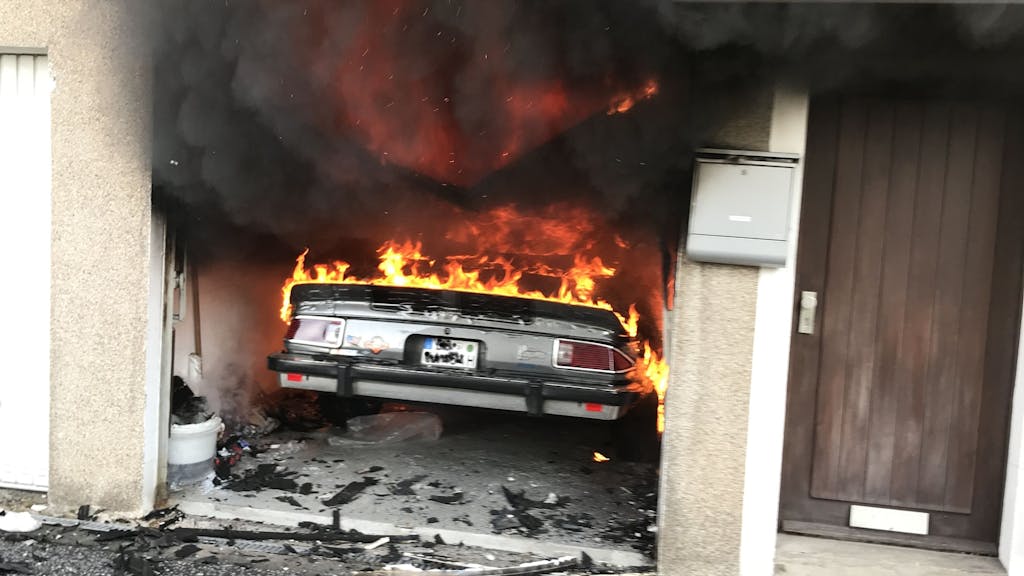Flammen schlagen aus einem Auto, das in einer Garage steht.