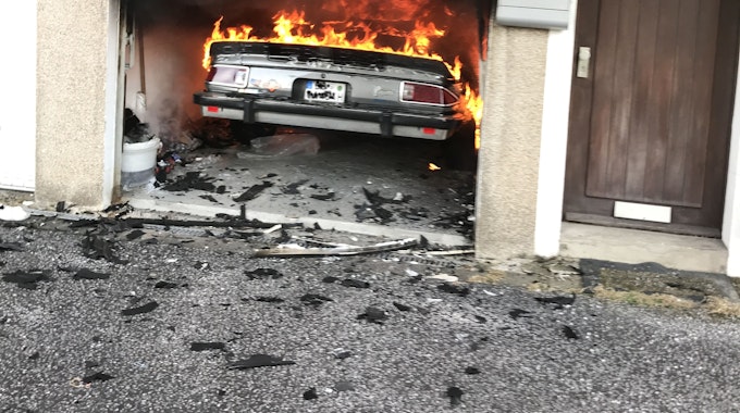 Flammen schlagen aus einem Auto, das in einer Garage steht.