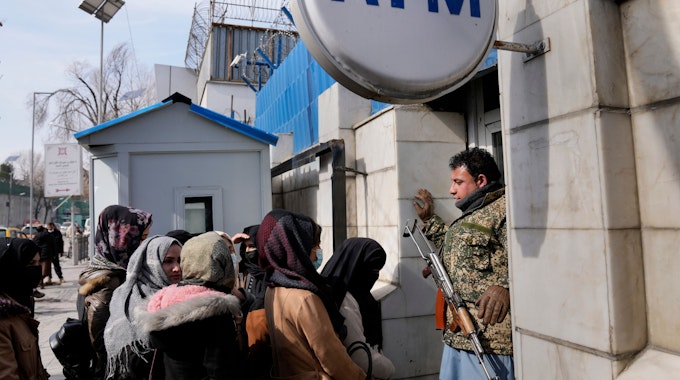 Ein afghanischer Sicherheitsbeamter mit einem AK-47 Gewehr steht vor einer Gruppe Frauen, die an einem Geldautomaten anstehen.