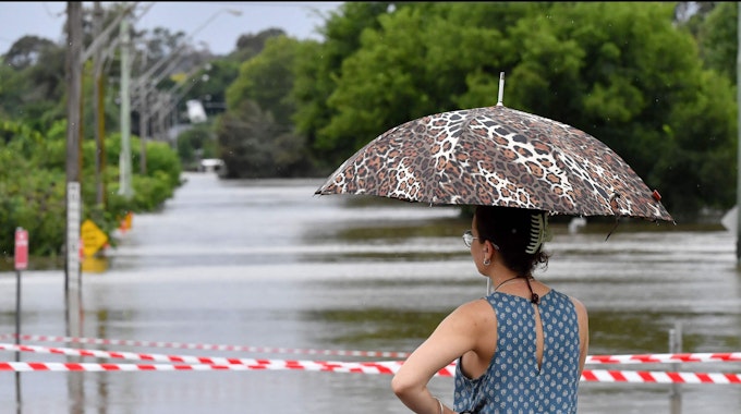 Eine Frau steht mit Schirm vor den überfluteten Straßen von Sydney. Heftige Unwetter suchen die australische Metropole heim.