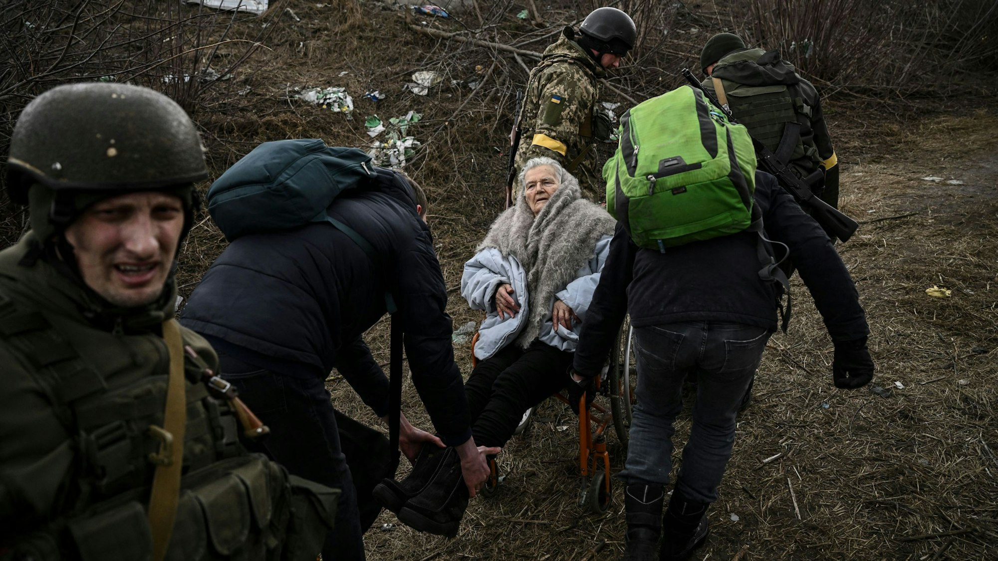 Menschen helfen einer älteren Frau im Rollstuhl, als sie am 7. März aus der Stadt Irpin westlich von Kiew fliehen. Die Lage in der Ukraine spitzt sich weiter zu.