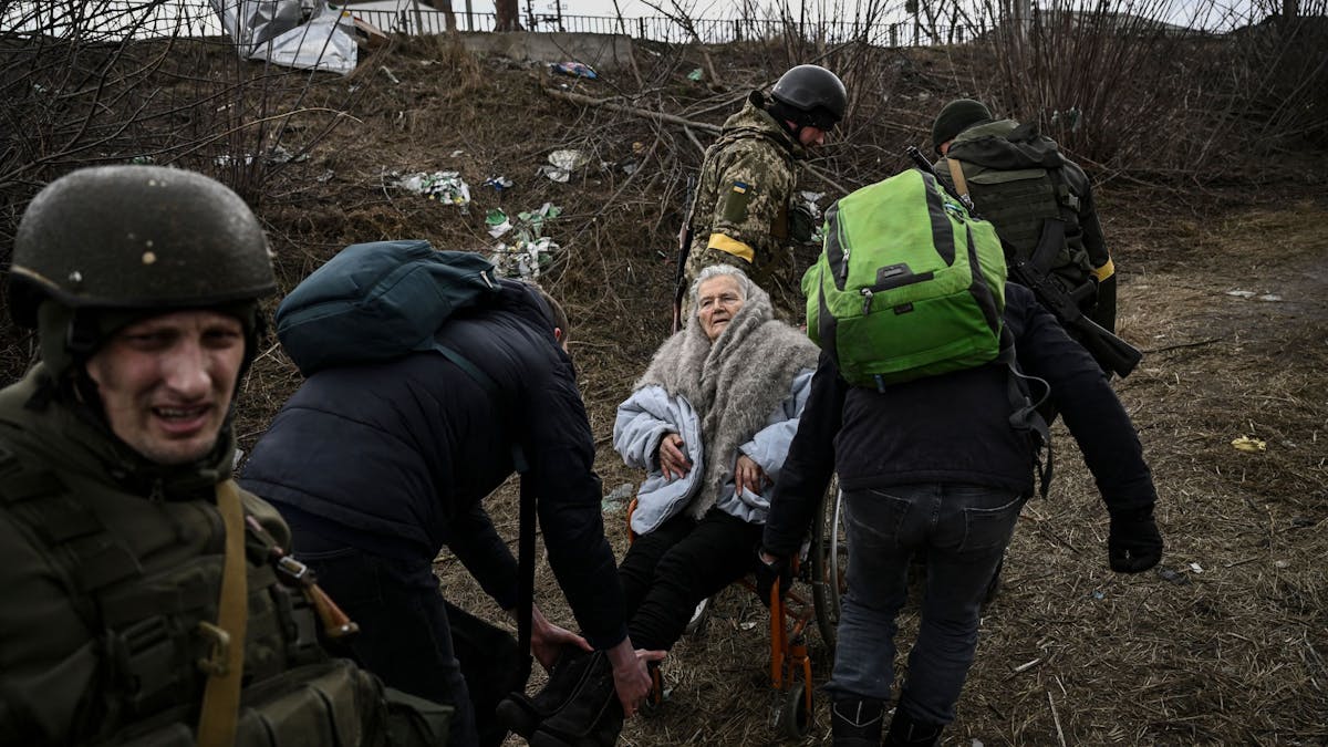 Menschen helfen einer älteren Frau im Rollstuhl, als sie am 7. März aus der Stadt Irpin westlich von Kiew fliehen. Die Lage in der Ukraine spitzt sich weiter zu.
