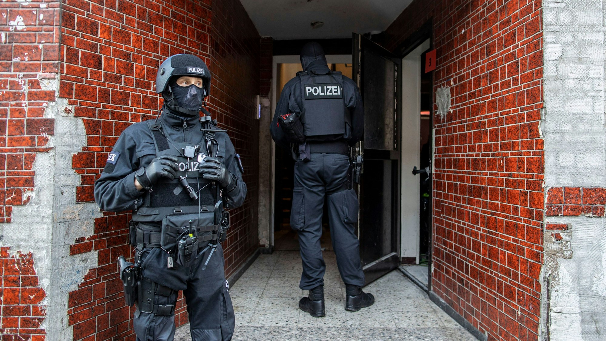 Polizisten stehen bei einer Razzia in einem Hauseingang.