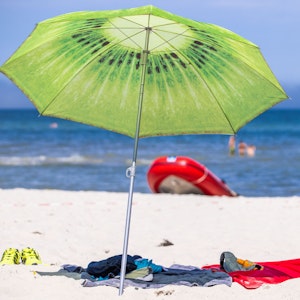 Ein grüner Sonnenschirm steht am Strand an der Ostseeküste.