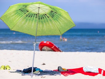 Ein grüner Sonnenschirm steht am Strand an der Ostseeküste.