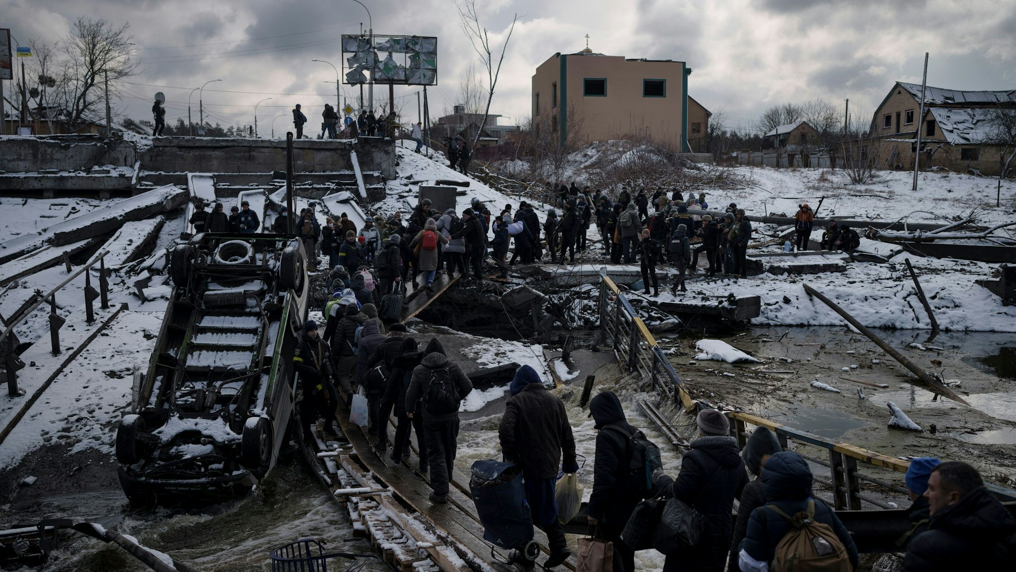 Ukrainische Männer und Frauen überqueren auf der Flucht aus Irpin einen behelfsmäßigen Weg zwischen den Trümmern einer zerstörten Brücke.