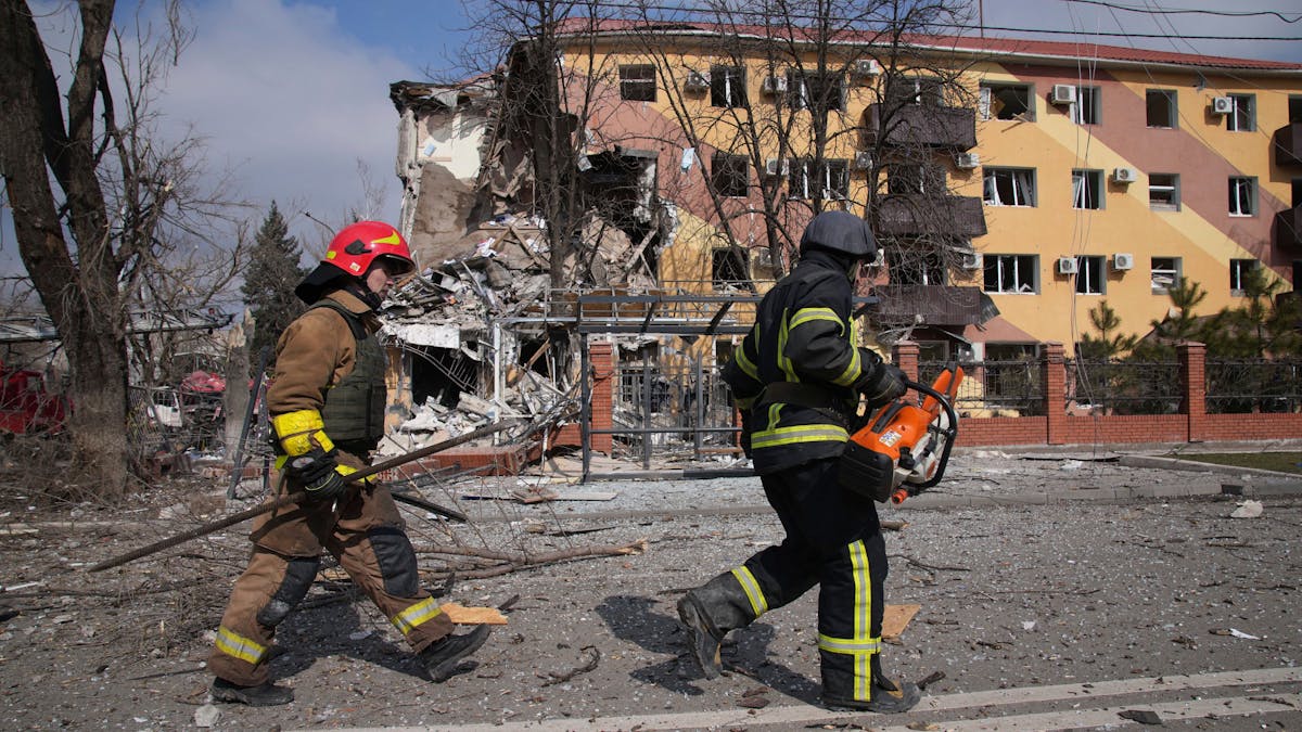 Feuerwehrleute gehen an einem durch Beschuss beschädigten Gebäude in Mariupol vorbei