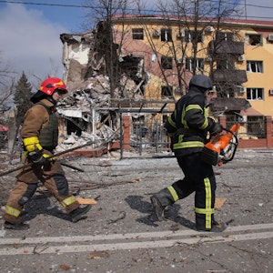 Feuerwehrleute gehen an einem durch Beschuss beschädigten Gebäude in Mariupol vorbei