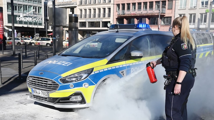 Eine Polizistin zielt mit einem Feuerlöscher auf das Rad eines Streifenwagens..