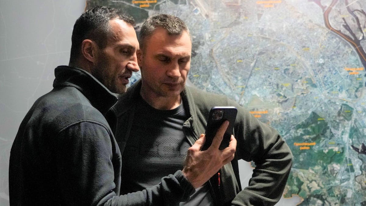 Wladimir (l.) und Vitali Klitschko schauen in einem Büro in Kiew auf ein Handy.