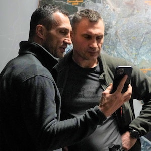 Wladimir (l.) und Vitali Klitschko schauen in einem Büro in Kiew auf ein Handy.
