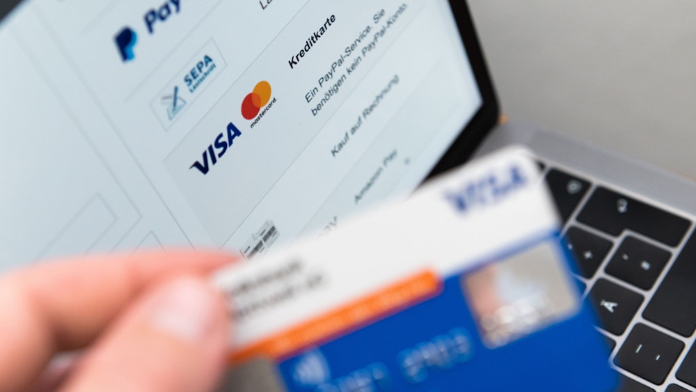 Ein Mann hält seine Kreditkarte in der Hand, während auf dem Bildschirm eines Laptops verschiedene Bezahlmethoden abgebildet sind.
