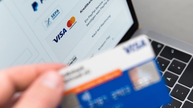 Ein Mann hält seine Kreditkarte in der Hand, während auf dem Bildschirm eines Laptops verschiedene Bezahlmethoden abgebildet sind.