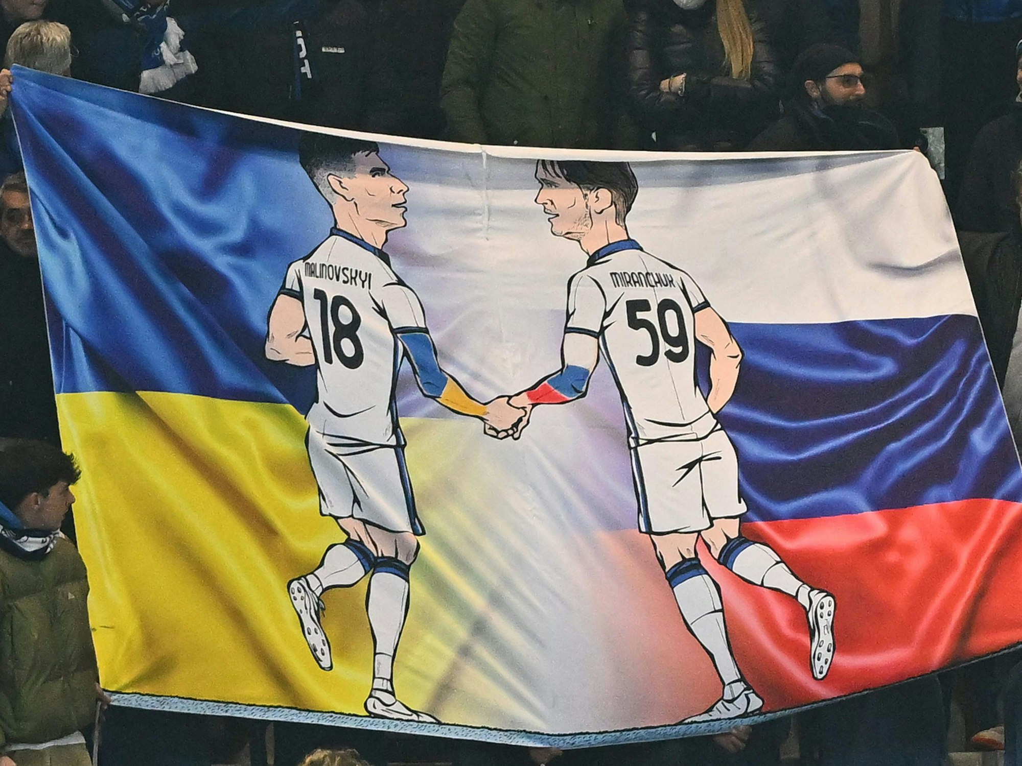Zeichnungen der Atalanta-Profis Ruslan Malinowskyi und Alexej Mirantschuk beim Europa-League-Spiel zwischen Bergamo und Bayer Leverkusen. Im Hintergrund des Banners sind die Landesflaggen der Ukraine und Russlands zu sehen.