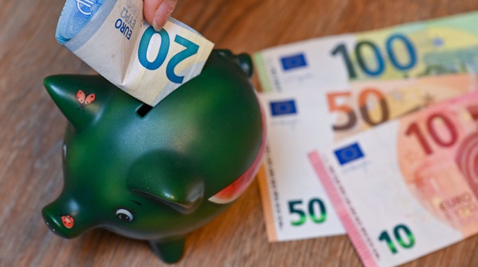 Ein Mädchen steckt einen 20-Euro-Schein in ein Sparschwein.
