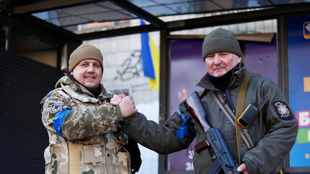 Zwei ukrainische Soldaten geben einander einen Handschlag, als sie auf einer Straße stehen. Bei nächtlichen russischen Angriffen am 15.03.2022 auf Ziele in der Ukraine sind nach Angaben aus Kyjiw mehrere Zivilisten getötet worden.