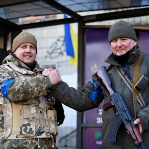 Zwei ukrainische Soldaten geben einander einen Handschlag, als sie auf einer Straße stehen. Bei nächtlichen russischen Angriffen am 15.03.2022 auf Ziele in der Ukraine sind nach Angaben aus Kyjiw mehrere Zivilisten getötet worden.