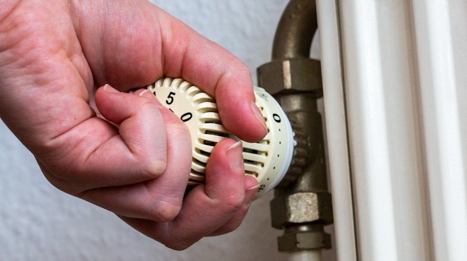 Eine Person dreht am Thermostat einer Heizung in einer Wohnung.
