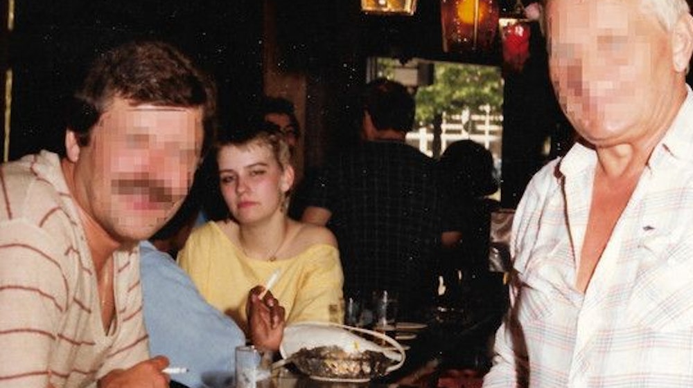 Eine junge Frau und ein Mann mit Schnäuzer sitzen an einem Kneipentresen, dahinter steht ebenfalls ein Mann. Die Gesichter der beiden Männer sind unkenntlich gemacht.