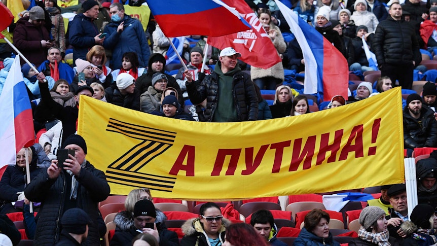 Tausende feiern in Moskau, während Putin seine Kriegsrede hält. Auf der Flagge steht das Kriegssymbol „Z“ geschrieben und „Für Putin“.