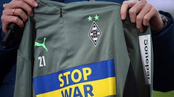 Um dieses schöne Stück geht es. Die Aufwärmshirts von Borussia Mönchengladbach mit der Botschaft „Stop War“ stehen noch zur Auktion. Das Shirt wird in die Kamera präsentiert.