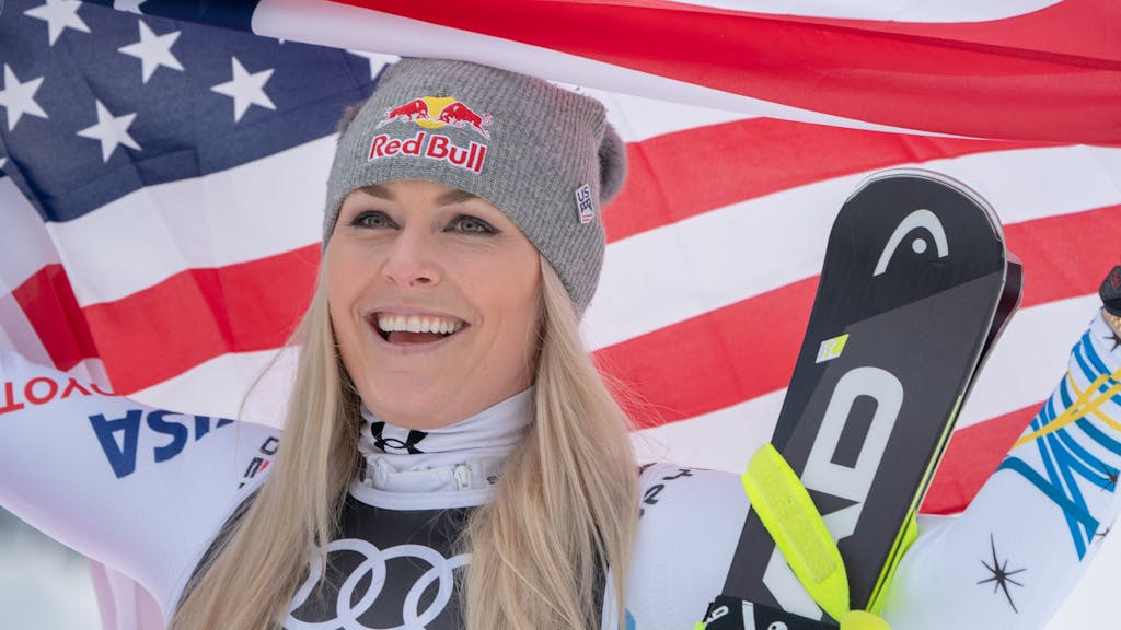Lindsey Vonn hält amerikanische Flagge hoch und lächelt.