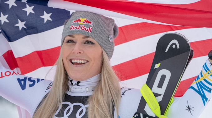 Lindsey Vonn hält amerikanische Flagge hoch und lächelt.