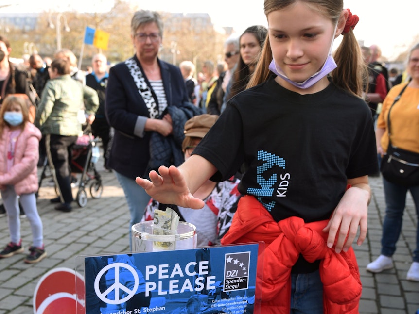 Ein Mädchen wirft Geld in eine Spendensäule auf der Peace-Please-Demo am Heumarkt.
