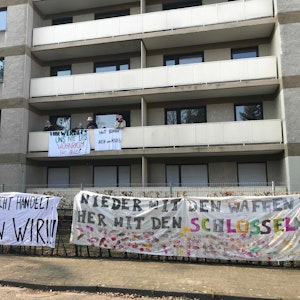Vier Männer haben ein Gebäude besetzt, sie befinden sich auf einem der Balkone. Am Balkon und am Zaun hängen Banner mit der Aufschrift „Nein zum Krieg“ und „Nieder mit den Waffen! Her mit den Schlüsseln!“
