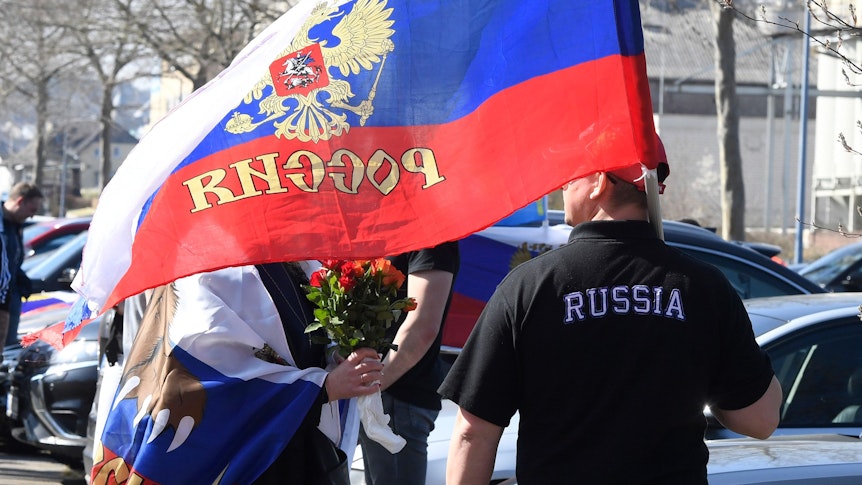 Mann geht mit russischer Fahne an einer Straße entlang.