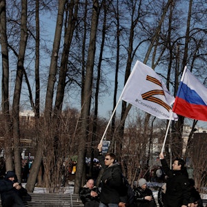Russische Männer halten Fahnen mit der Nationalflagge und dem Kriegssymbol Z hoch.
