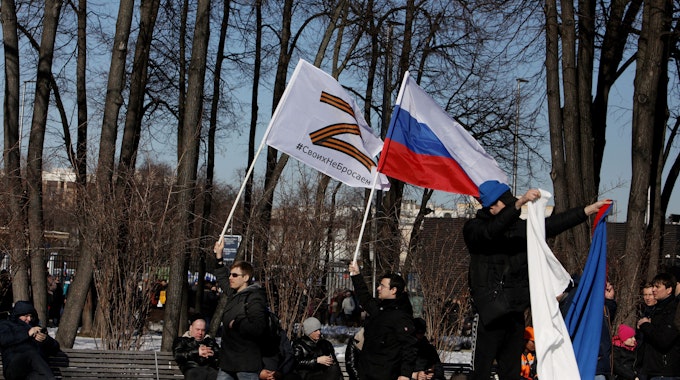 Russische Männer halten Fahnen mit der Nationalflagge und dem Kriegssymbol Z hoch.
