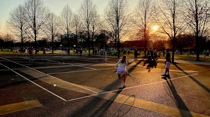 Menschen spielen in der Abendsonne auf einem öffentlichen Tennisplatz.
