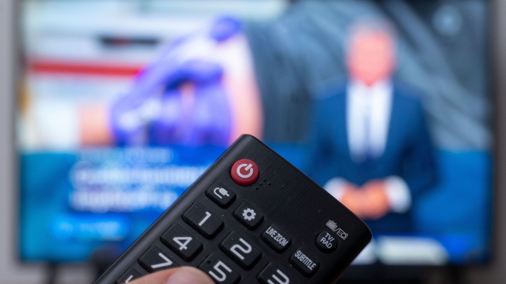 Ein Mann hält eine Fernbedienung vor einen Fernseher, auf dem die ARD-„Tagesschau“ läuft