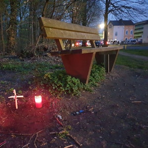 Ein Kreuz und zwei Kerzen stehen neben einer Sitzbank.