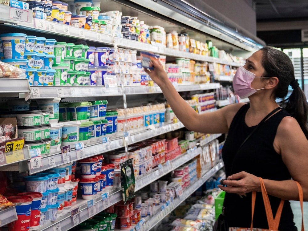 Eine Frau mit Mund-Nasen-Bedeckung steht vor einem Kühlregal im Supermarkt.