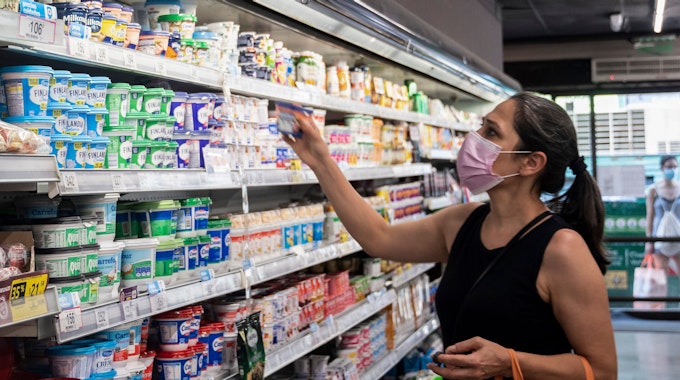 Eine Frau mit Mund-Nasen-Bedeckung steht vor einem Kühlregal im Supermarkt.