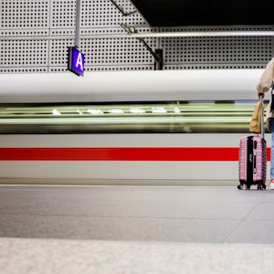 Frau steht mit Koffern an Bahnsteig, ICE fährt durch.