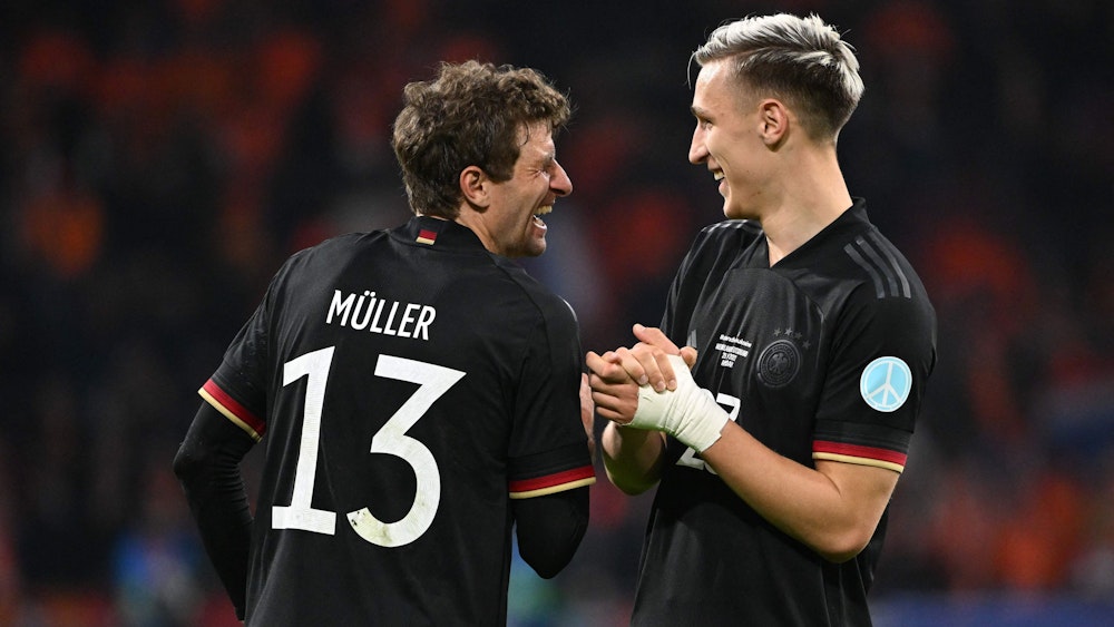 Thomas Müller und Nico Schlotterbeck lachen zusammen auf dem Platz.