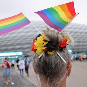 Eine Fußball-Anhängerin mit zwei kleinen Regenbogenfahnen im Haar steht vor der Münchner Allianz-Arena.