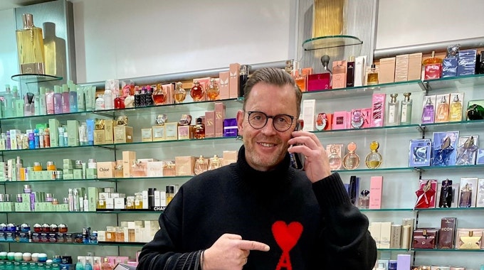 Heinz-Josef Meller steht mit Telefon und Einkaufstüten in seiner Parfümerie Meller in Köln.
