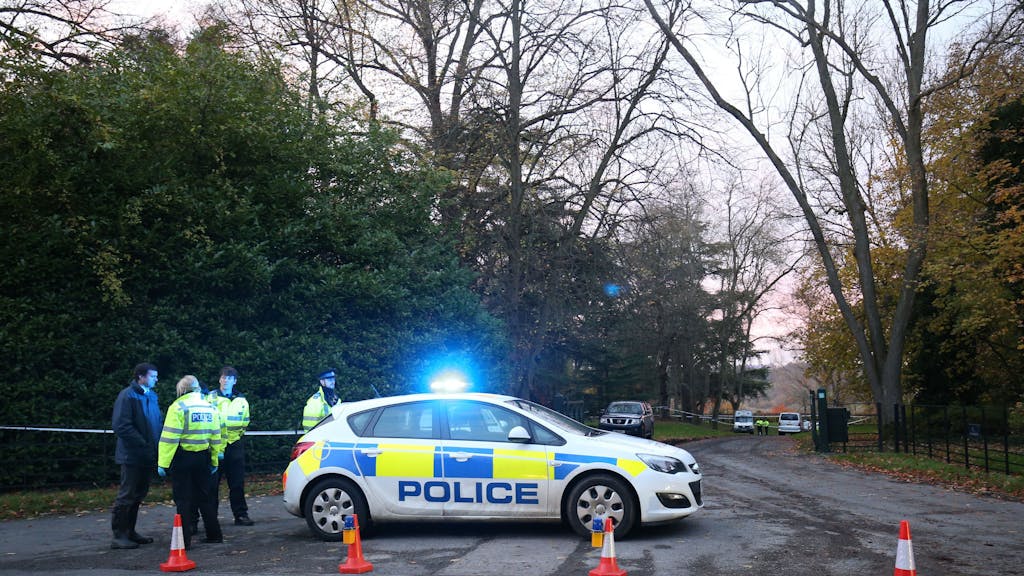 Ein englisches Polizeiauto steht auf einer Straße. Daneben steht ein Polizist.