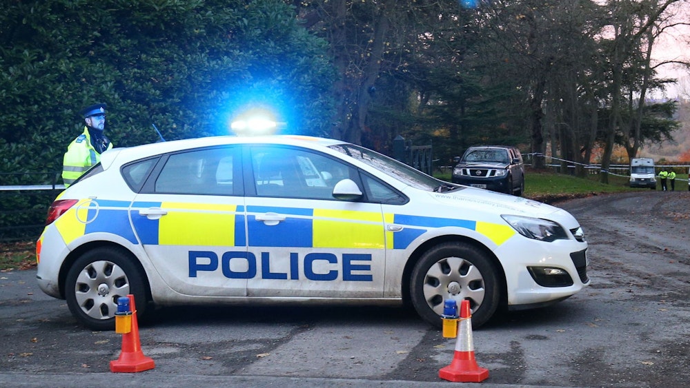 Ein englisches Polizeiauto steht auf einer Straße. Daneben steht ein Polizist.