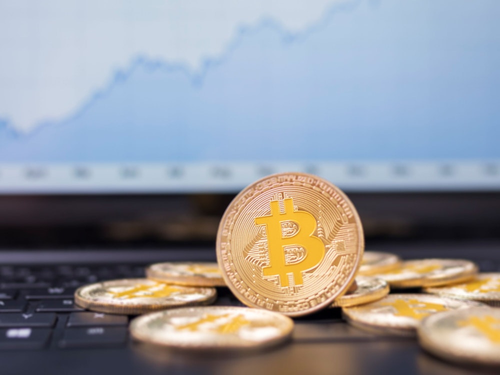 Münzen mit dem Bitcoin-Logo liegen auf der Tastatur eines Laptops.