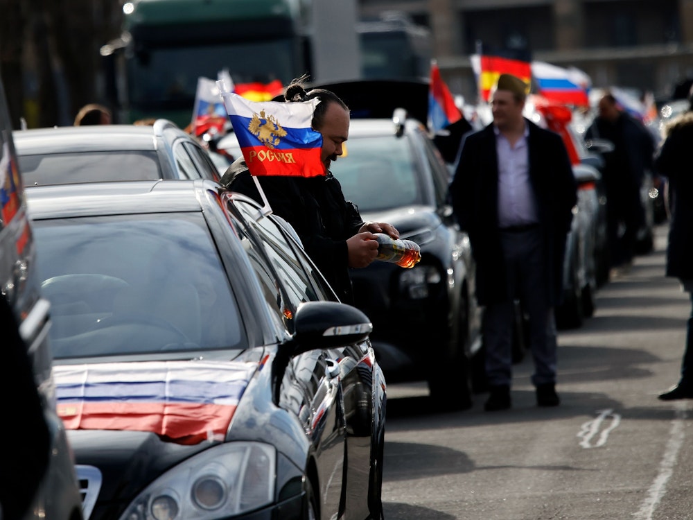 Flaggen mit den russischen Nationalfarben und dem russischen Staatswappen wehen an einem Auto auf dem Olympiaplatz vor dem Olympiastadion. Etwa 900 Menschen haben am Sonntag in Berlin an einem Autokorso mit russischen Fahnen teilgenommen.