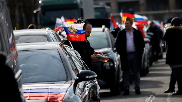 Flaggen mit den russischen Nationalfarben und dem russischen Staatswappen wehen an einem Auto auf dem Olympiaplatz vor dem Olympiastadion. Etwa 900 Menschen haben am Sonntag in Berlin an einem Autokorso mit russischen Fahnen teilgenommen.