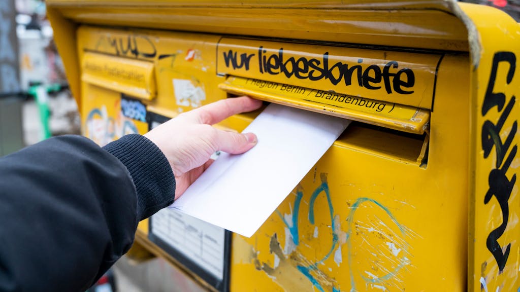 Eine Person wirft einen Brief in einen Briefkasten.