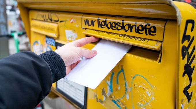 Eine Person wirft einen Brief in einen Briefkasten.