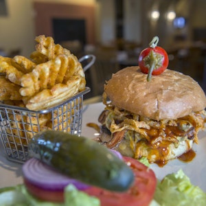 Ein Barbecue-Burger mit Speck und gerösteten Zwiebeln steht neben Gitter-Pommes auf dem Tisch.
